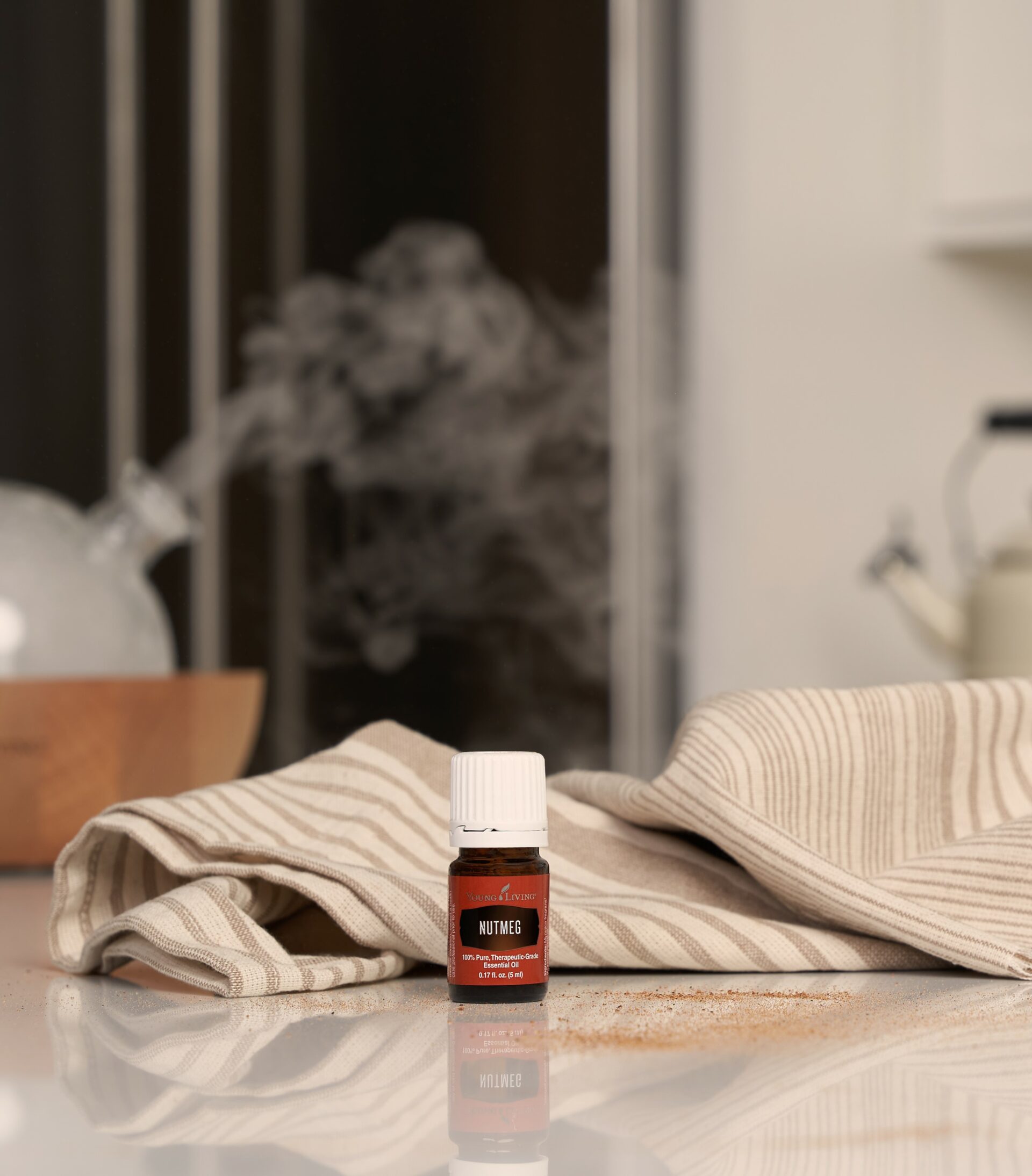 Nutmeg Essential Oil sitting on countertop with kitchen towel and Aria diffuser in background - Young Living Lavender Life Blog 