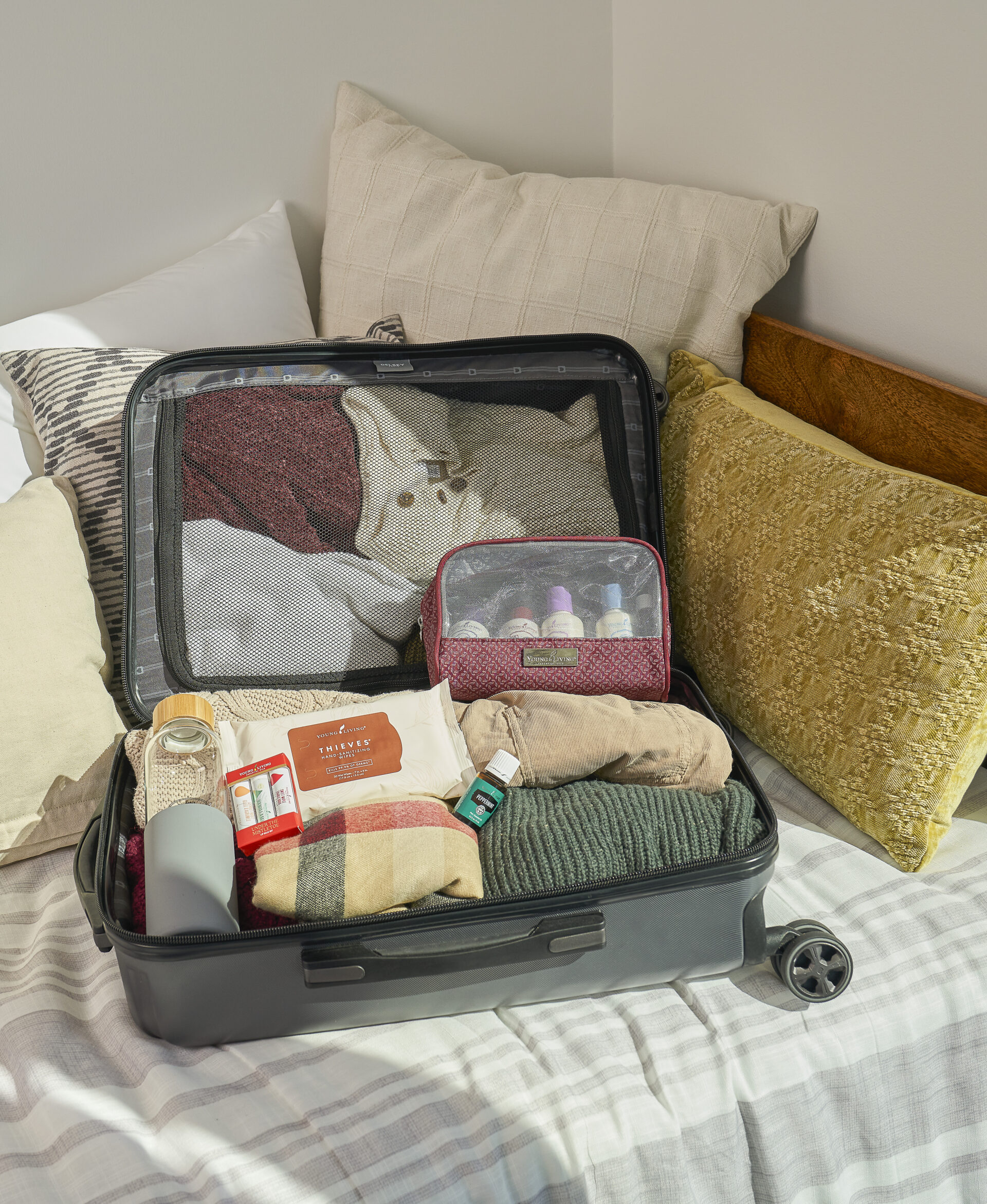 Suitcase sitting on bed with water bottle, Thieves Hand Sanitizing Wipes, Under The Mistletoe Lip Balm Set, Peppermint Essential Oil, and Bon Voyage Travel Pack - Young Living Lavender Life blog 