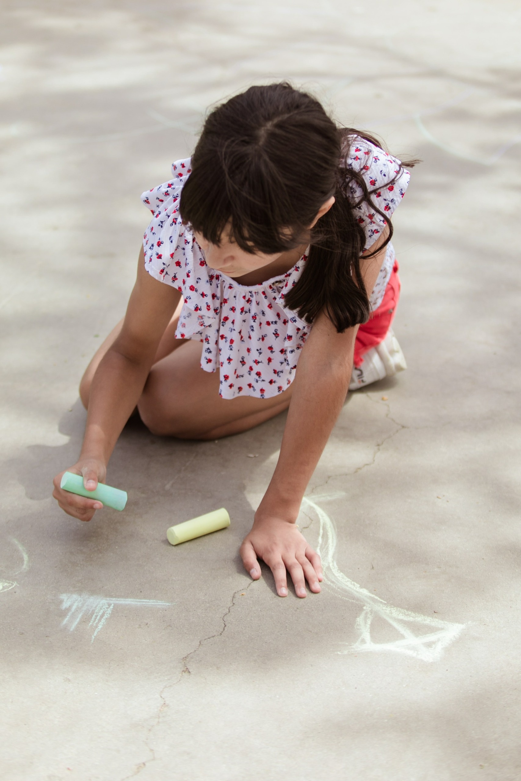 Little girl drawing with chalk on sidewalk 