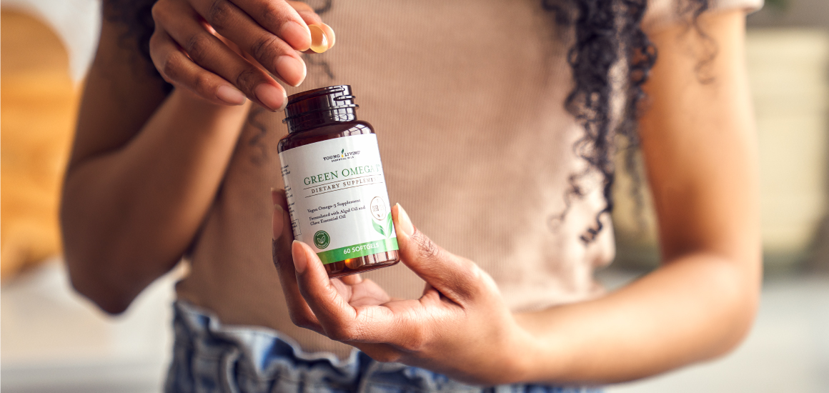 a pair of hands holding the green omega 3 supplement